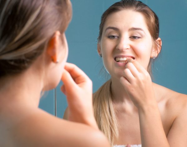 Young woman cleaning and checking her teeth at mirror in bathroom Young woman cleaning and checking her teeth at mirror in bathroom.
